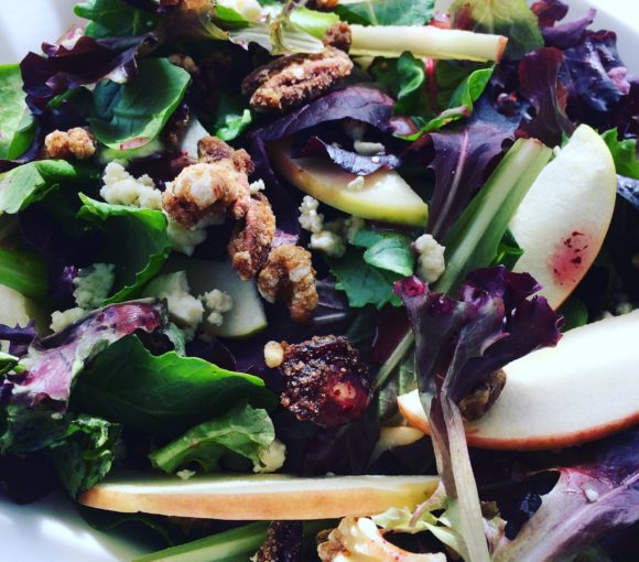 Salad featuring mixed greens with baby kale, pink lady apples, gorgonzola cheese, pecans, walnuts, and raspberry walnut dressing.